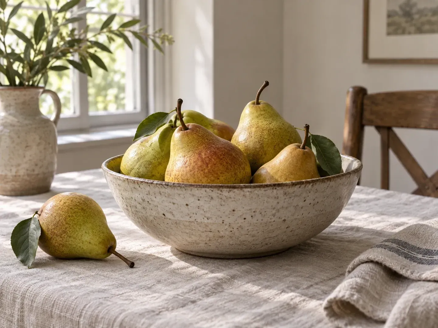 A ceramic bowl of pears on a linen-covered table in soft natural window light